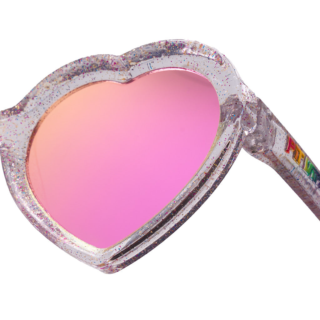 Close-up of heart-shaped sunglasses with a glittery silver frame and a pink mirrored lens, on a white background.