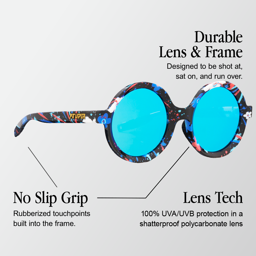 Infographic for Pit Viper Freedom Ring Mooner sunglasses showing a side/angled view of oversized round sunglasses with a black frame covered in blue, white, and red paint-splatter print, blue mirrored round lenses, and a gold 'PIT VIPER' logo on the temple arm with 3 callouts: 'Durable Lens & Frame - Designed to be shot at, sat on, and run over.', 'No Slip Grip - Rubberized touchpoints built into the frame.', 'Lens Tech - 100% UVA/UVB protection in a shatterproof polycarbonate lens'