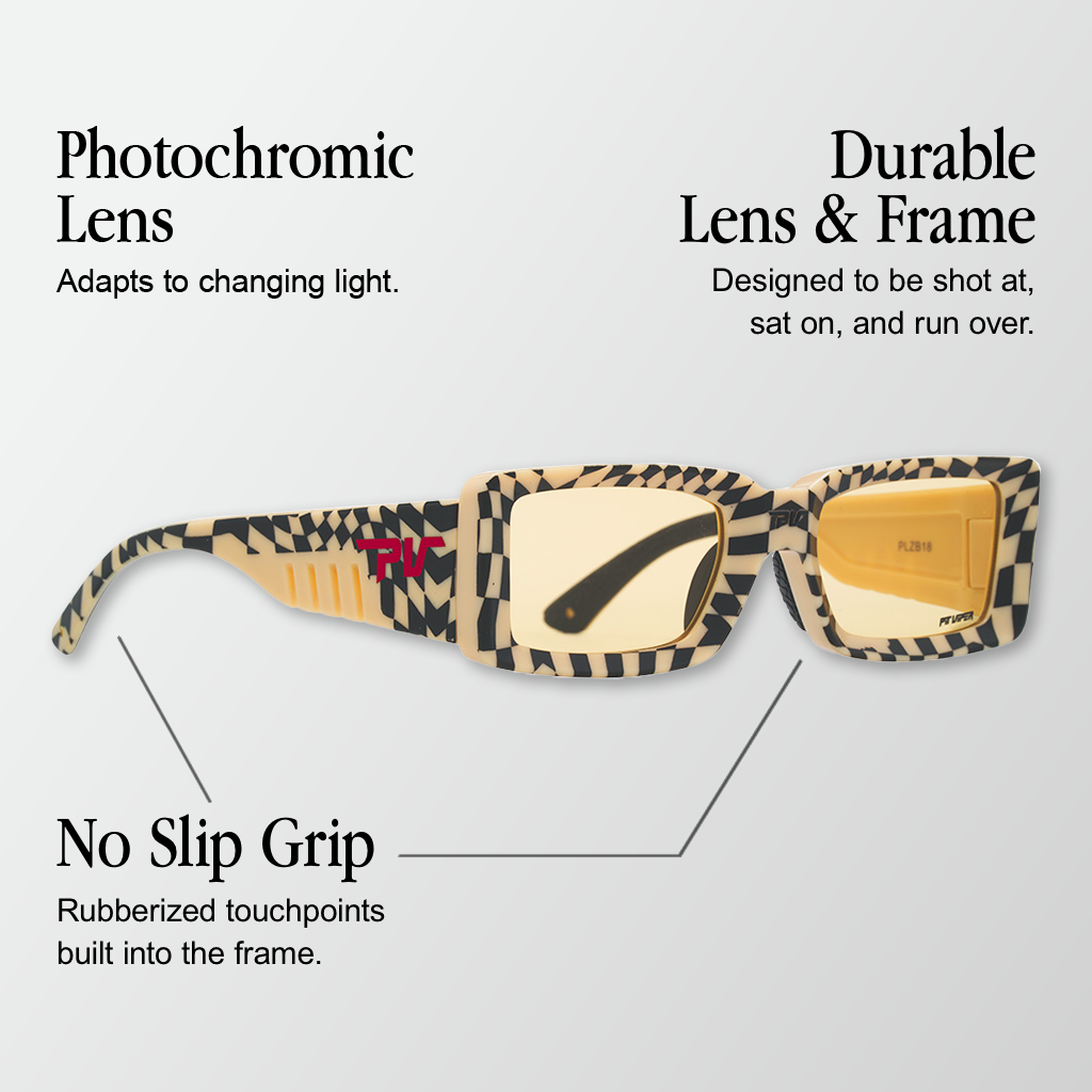 Infographic for Pit Viper Low Bones photochromic sunglasses showing a side/angled view of a narrow rectangular retro-style frame in a black-and-cream checkerboard print, a light amber photochromic lens, a red 'PV' logo on the temple, and 'PIT VIPER' text on the lens with 3 callouts: 'Photochromic Lens - Adapts to changing light.', 'Durable Lens & Frame - Designed to be shot at, sat on, and run over.', 'No Slip Grip - Rubberized touchpoints built into the frame.'