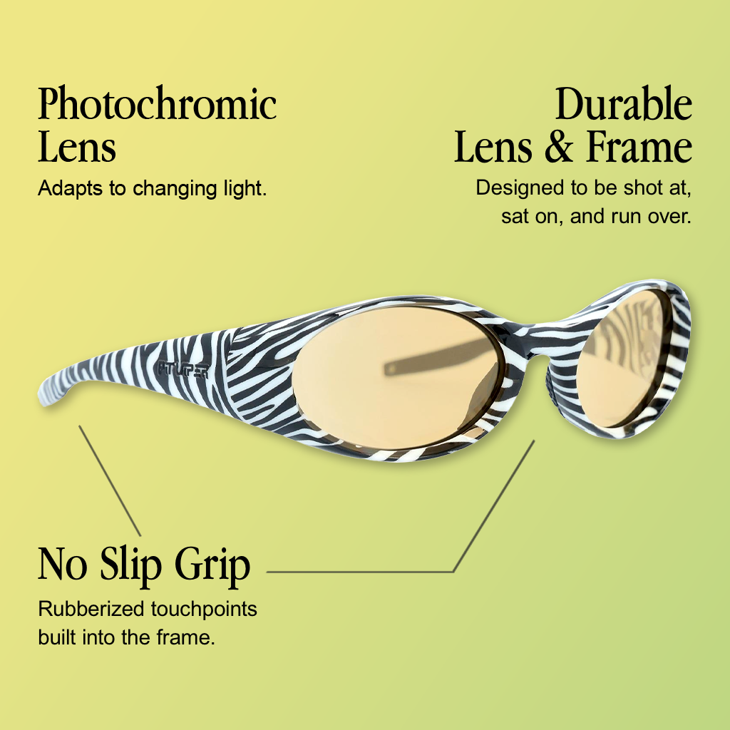 Infographic for Pit Viper Slammer Poc sunglasses showing a side/three-quarter view of black-and-white zebra-print oval frames with an embossed 'PIT VIPER' logo on the temple and an amber/tan photochromic lens, on a yellow-green gradient background, with 3 callouts: 'Photochromic Lens - Adapts to changing light.', 'Durable Lens & Frame - Designed to be shot at, sat on, and run over.', 'No Slip Grip - Rubberized touchpoints built into the frame.'